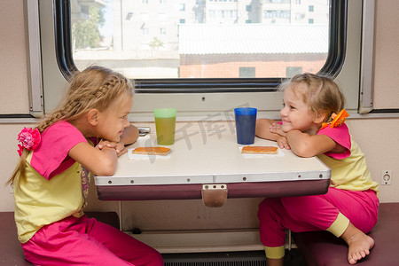 火车上两个小女孩满脸幸福地看着对方，坐在舷外二等车厢的桌子旁