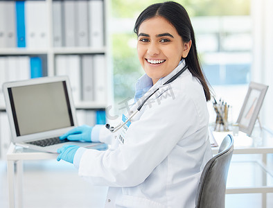医生，微笑着，与医疗保健员工在医院咨询室或办公室的办公桌前一起制作笔记本电脑模型。