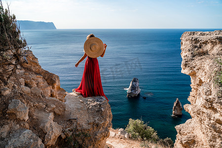 红长袍摄影照片_身着飘扬红裙、头戴草帽的女子，映衬在大海的映衬下。