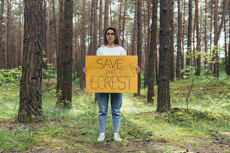 保护环境海报摄影照片_年轻女子在树林纠察队做志愿者，举着拯救森林的海报