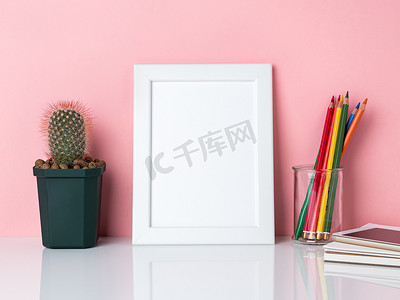空白的白框，罐子里的蜡笔，在白桌上种植仙人掌，靠在粉红色的墙上，有复制空间