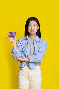 哭泣的亚洲女孩拿着紫色的信用卡，借记卡上带着悲伤、不快乐的脸乞讨钱。