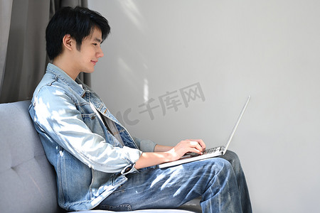 微笑的男人坐在明亮的客厅里，在笔记本电脑上查看电子邮件。