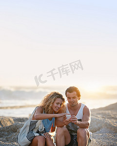 日落时在海滩上使用智能手机的年轻夫妇