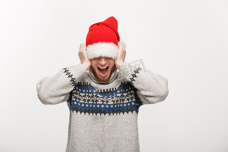 假日概念-穿着毛衣的年轻胡子男人喜欢玩圣诞老人的帽子。