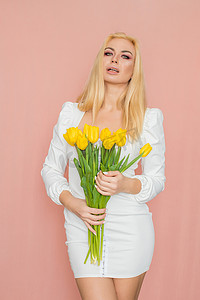 白裙摄影照片_身穿春白裙的金发女人手里拿着花束