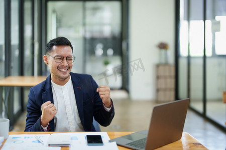 幸福感摄影照片_一位亚洲男性企业主站在电脑前的肖像，在成功投资后表现出幸福感