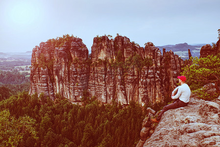 岩石上戴着红帽的男子徒步旅行者看着尖锐的山