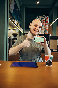 坐在现代咖啡馆附近的长椅上，快乐的男性用手指指着空白的平板电脑蓝屏