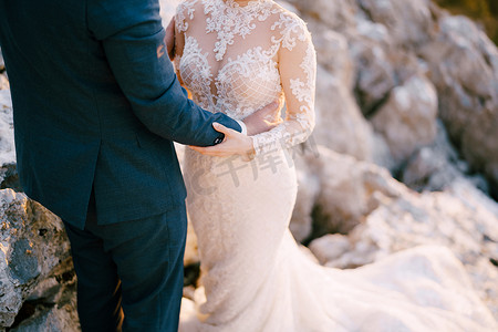 长腰摄影照片_新郎站在石头上搂着新娘的腰。