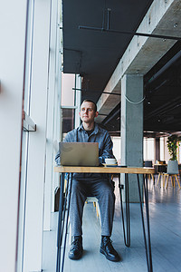 一位身穿西装的年轻成功商人喝着咖啡，在咖啡馆里用笔记本电脑无线免费上网工作，独自坐在咖啡馆的桌子旁。