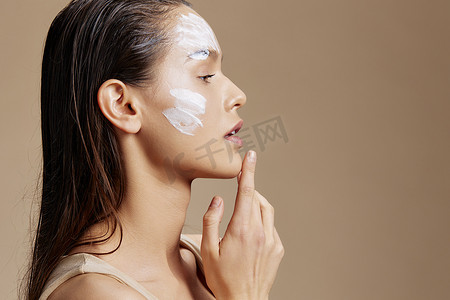 年轻女子面膜霜清洁皮肤面部磨砂米色背景