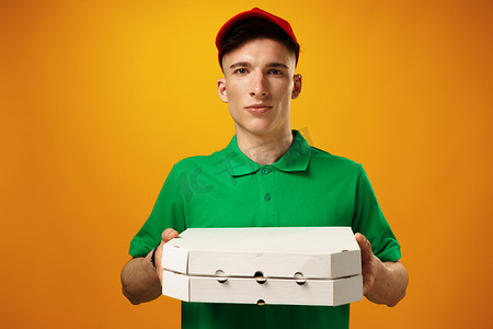 黄色背景下拿着披萨盒的快乐年轻送货员