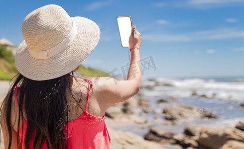 夏日拍照摄影照片_戴帽子的女人在海上拍照，拉丁女孩在度假拍照，女孩在沙滩上自拍的后视