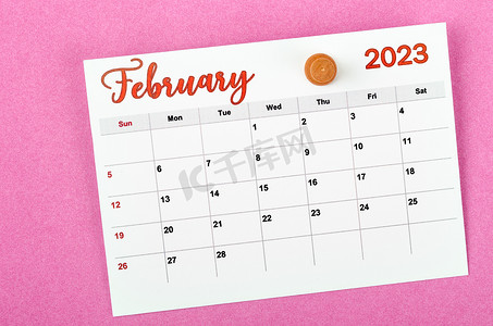 2023 年 2 月月历，粉红色背景上带有木制图钉。