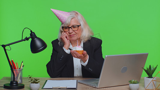 独自庆祝生日派对的悲伤而沮丧的孤独高级女商人在绿色办公室拿着蛋糕