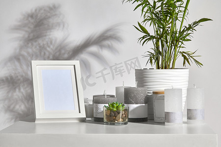带阴影的相框摄影照片_桌子上放着绿色植物和多汁植物，有不同大小和颜色的蜡烛、相框、带木盖的罐子。