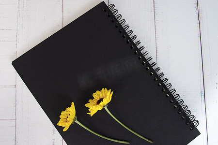 向日葵书摄影照片_黑色笔记本平铺在木桌上，上面放着向日葵。