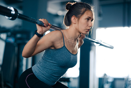 有魅力的年轻运动女性在健身房里用杠铃深蹲。