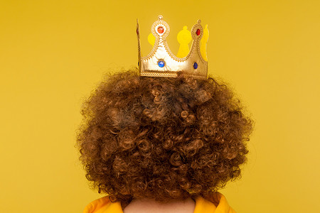 卷发背面摄影照片_背面肖像卷发女孩在黄色背景与皇冠。