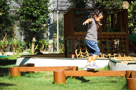 活跃的小女孩在公园的室外操场上走在平衡木上。