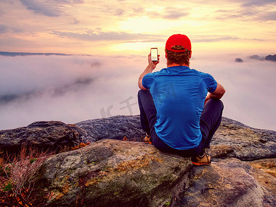 勇敢的男人坐在岩石顶上用手机拍照