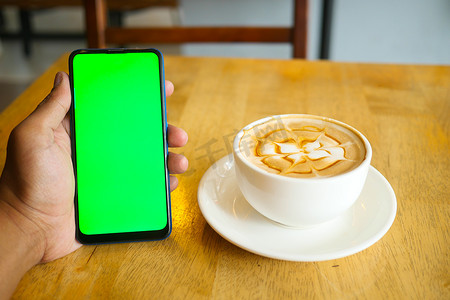 手机花屏摄影照片_拿着一杯咖啡，使用带绿屏的智能手机