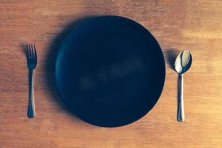 木桌上有勺子和叉子的空黑盘的顶部视图
