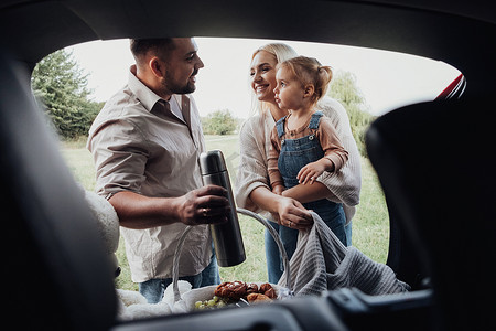 年轻的家庭，两个父母带着他们的小孩准备在户外野餐，透过 SUV 汽车的敞开后备箱观看