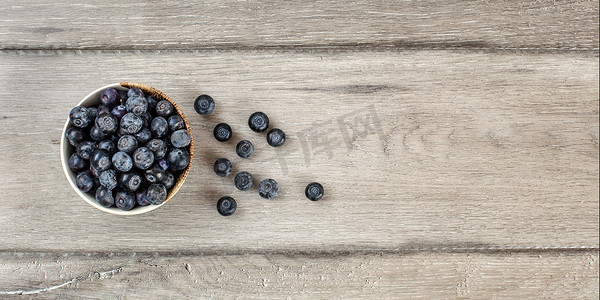 桌面视图 — 装有蓝莓的小碗，其中一些洒在灰色木桌上。