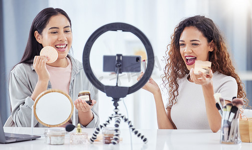 两名混血女性坐在家里用手机为她们的美容博客录制化妆教程。