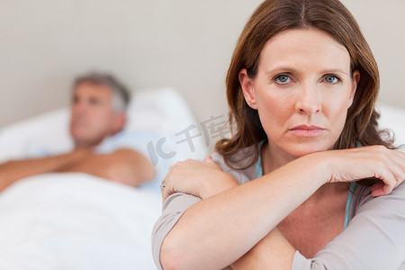 年代感卧室摄影照片_悲伤的女人躺在床上，背景是丈夫