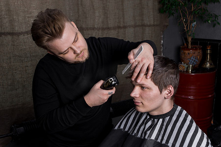 理发师或美发师的手在理发店里用自动机器和梳子给深色头发的顾客剪发。