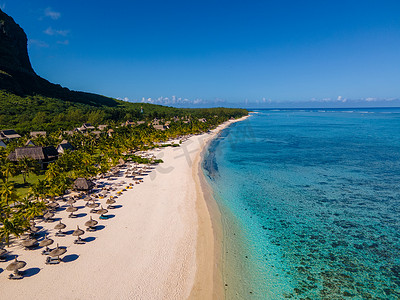 Le Morne 海滩毛里求斯，带棕榈树和白色沙滩蓝色海洋的热带海滩和带雨伞的沙滩床、太阳椅和遮阳伞在热带海滩的棕榈树下，Le Morne 海滩毛里求斯