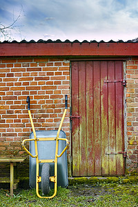 一个颠倒的手推车的镜头，一个带有红色和黄色混合油漆门的砖砌小农舍，以及湿草地上的一张木桌。