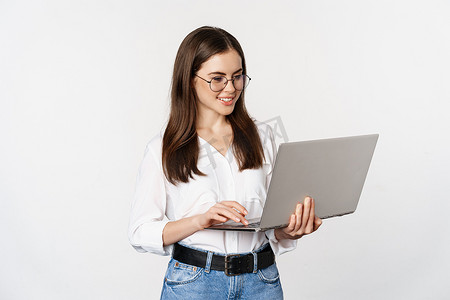 克蓝英蓝笑脸摄影照片_年轻办公室女性的画像，企业家在笔记本电脑上回答客户，用笑脸的电脑工作，站在白色背景上