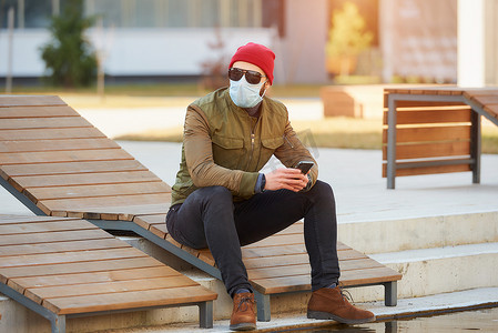 坐在木制躺椅上的家伙戴着墨镜和面罩来抵御病毒