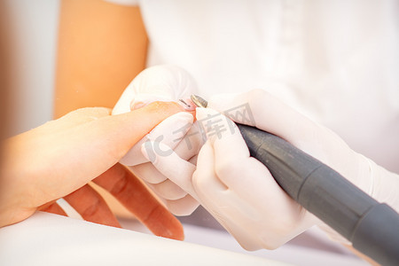 戴白手套的美甲大师在美容院用电动指甲锉钻去除指甲油的特写。