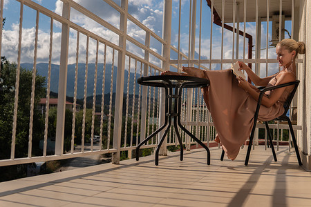 阳台人摄影照片_女孩坐在群山和蓝天的阳台上，背景是美丽的阳台美丽的女性，户外肖像外放松，家。