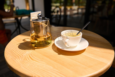 茶杯和玻璃茶壶，配有健康疗法和抗氧化凉茶，位于自助餐厅露台的木制圆桌上