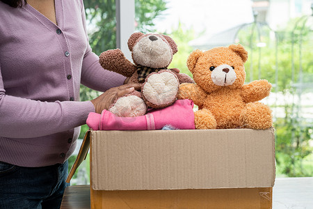 在家中拿着装有旧衣服和娃娃的衣物捐赠箱，以支持对世界上穷人的帮助。