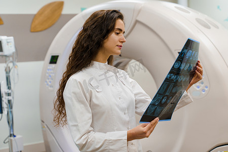 身穿医用长袍的年轻女医生在计算机断层扫描后查看患者大脑的 X 光照片。 