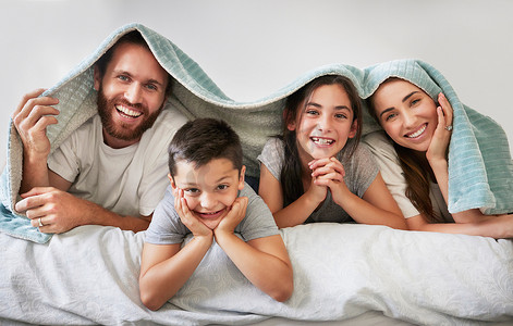 四口之家吃饭摄影照片_幸福的白人四口之家的肖像躺在床上，头上盖着毯子。