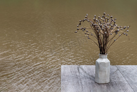 干花的复古色调图像在白色花瓶中用于装饰目的在旧木桌上以河景为背景。