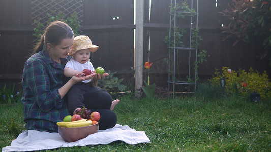 快乐年轻开朗的母亲抱着婴儿在绿草上吃水果。