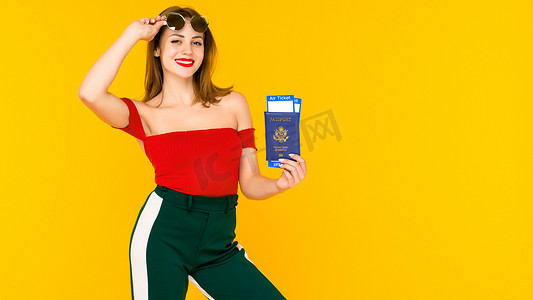 旅游黄色背景摄影照片_黄色背景中一位拿着旅行票和护照的快乐年轻女子的画像