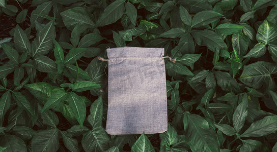 绿色灌木树叶背景上的空白样机亚麻棉手提袋。