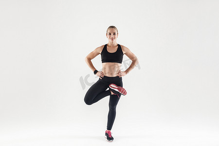 一条腿站立摄影照片_单腿站立，双手系腰带的运动女性