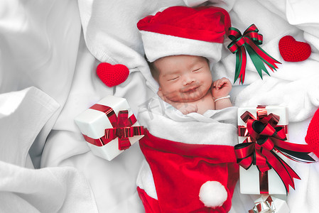 戴着圣诞帽、圣诞老人送的礼盒和白软毛巾上的纱心睡着的新生婴儿脸。