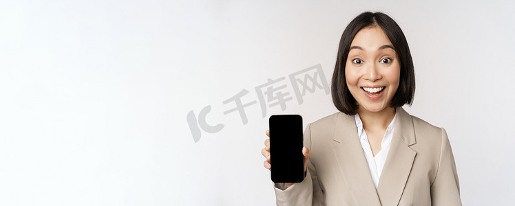 app展示界面摄影照片_亚洲企业女性展示应用程序界面、手机屏幕、做出惊讶的表情、哇，站在白色背景上